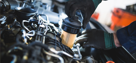 En hand som drar ut motoroljefiltret ur motorn